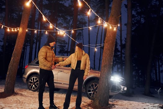 Automobile parked behind. Couple standing in the forest and celebrating New year.