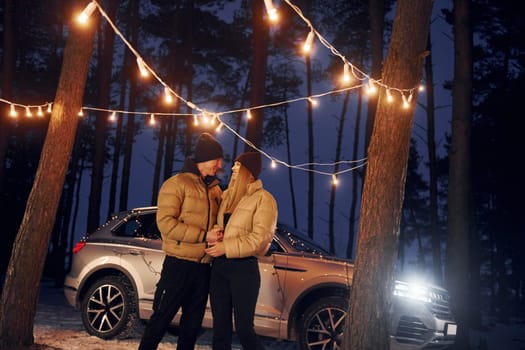 Car is at background. Couple standing in the forest and celebrating New year.