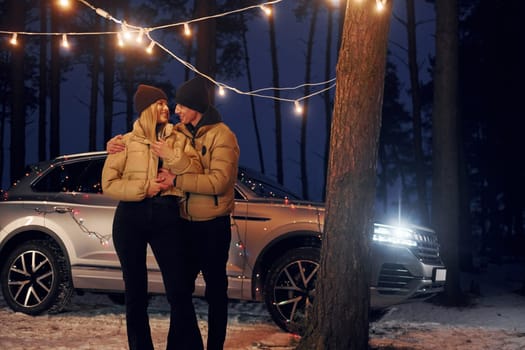 Car is at background. Couple standing in the forest and celebrating New year.
