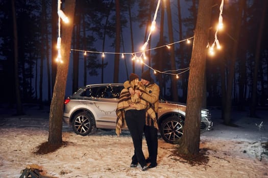 Car is at background. Couple standing in the forest and celebrating New year.