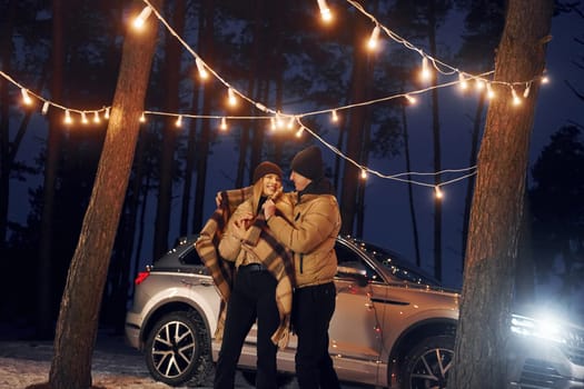 Car is at background. Couple standing in the forest and celebrating New year.