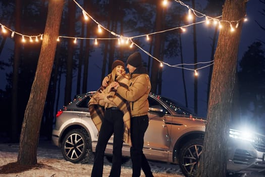 Car is at background. Couple standing in the forest and celebrating New year.