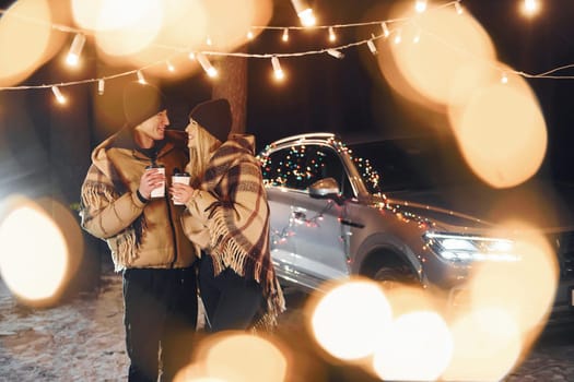 With warm drinks. Couple standing in the forest and celebrating New year.