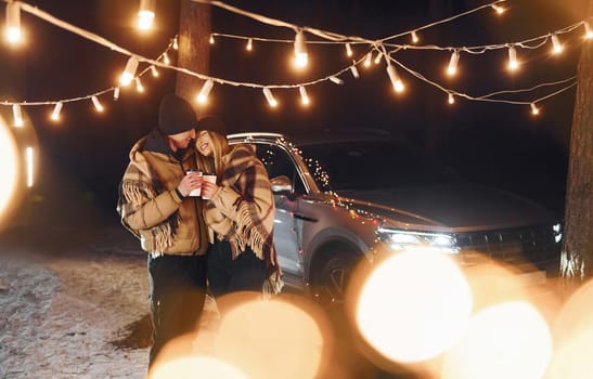 With warm drinks. Couple standing in the forest and celebrating New year.