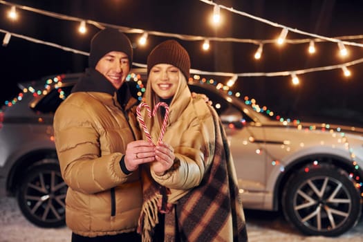 Holding candies. Couple standing in the forest and celebrating New year.