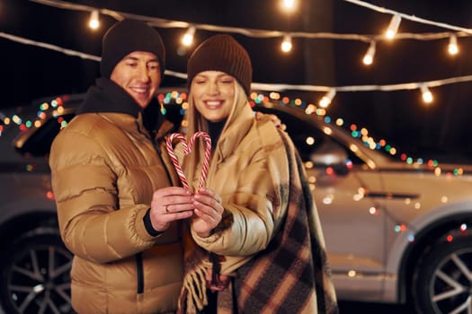 Holding candies. Couple standing in the forest and celebrating New year.