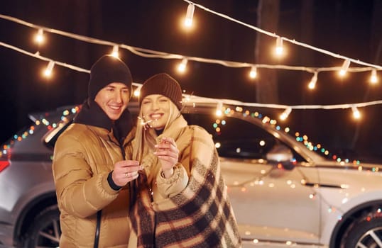 Holding sparklers. Couple standing in the forest and celebrating New year.