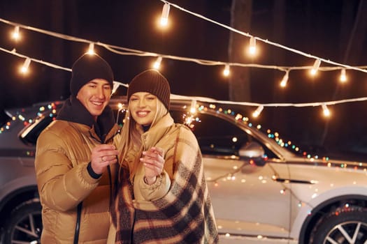 Holding sparklers. Couple standing in the forest and celebrating New year.