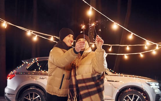 Holding sparklers. Couple standing in the forest and celebrating New year.