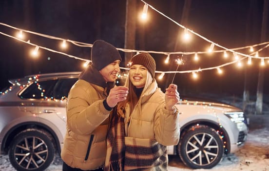 Holiday lights. Couple standing in the forest and celebrating New year.