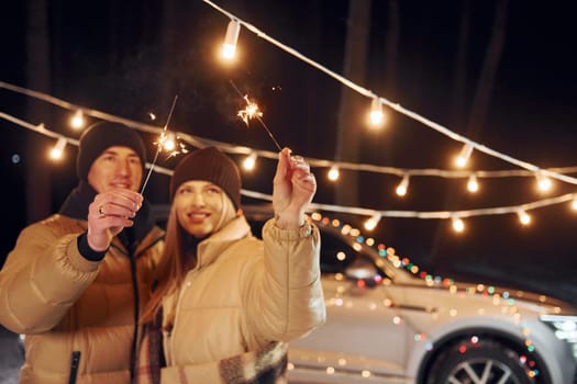 Holiday lights. Couple standing in the forest and celebrating New year.
