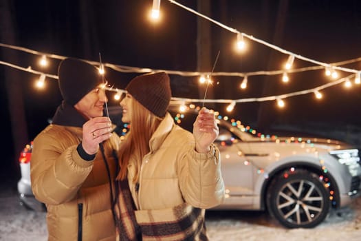 Holiday lights. Couple standing in the forest and celebrating New year.