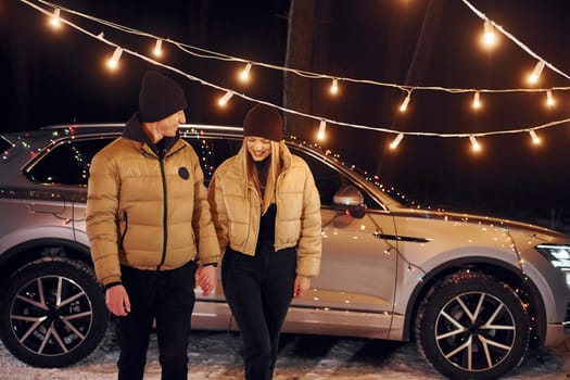 With modern car behind. Couple standing in the forest and celebrating New year.