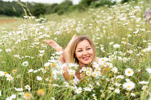 A woman lies in a chamomile field, dressed in a white dress.