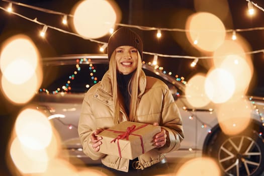 Holding gift box. Woman standing in the forest and celebrating New year.