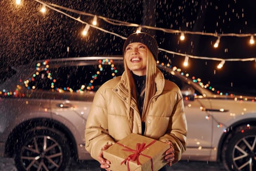 Smiling and holding gift. Woman standing in the forest and celebrating New year.
