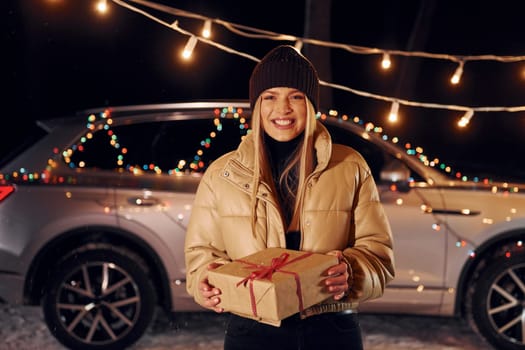 Smiling and holding gift. Woman standing in the forest and celebrating New year.