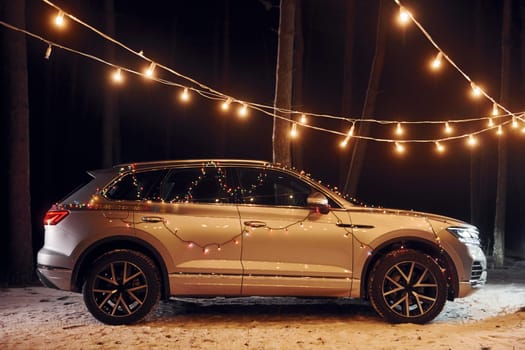 Side view. Modern silver colored automobile parked in forest with holiday decoration.