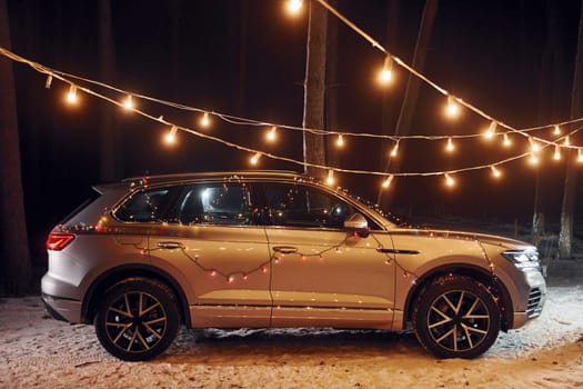 Side view. Modern silver colored automobile parked in forest with holiday decoration.