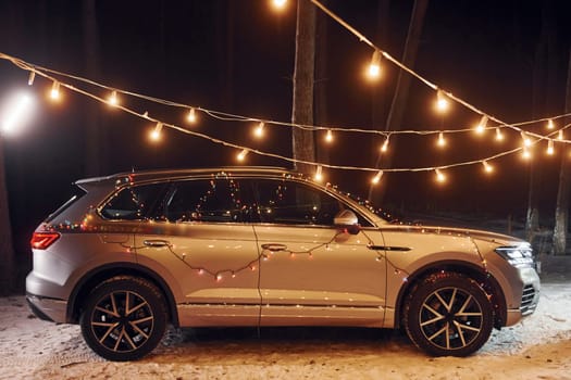 Side view. Modern silver colored automobile parked in forest with holiday decoration.