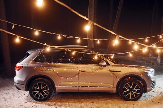 Side view. Modern silver colored automobile parked in forest with holiday decoration.