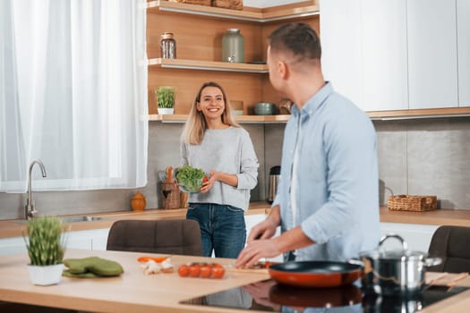 Man standing by the table. Couple preparing food at home on the modern kitchen.