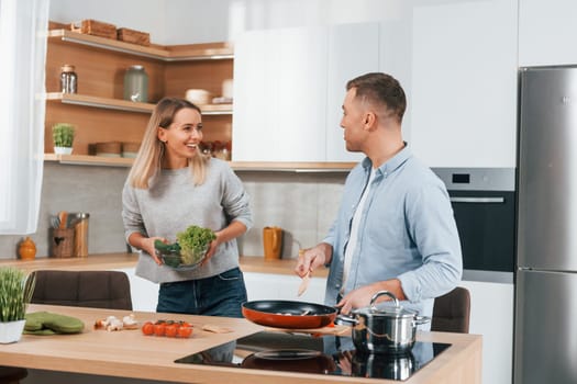 Talking with each other. Couple preparing food at home on the modern kitchen.
