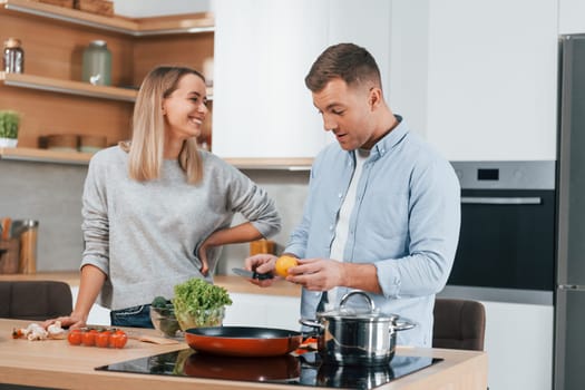 Talking with each other. Couple preparing food at home on the modern kitchen.