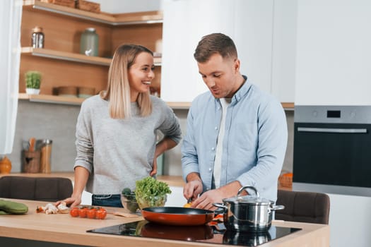 Talking with each other. Couple preparing food at home on the modern kitchen.