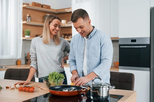 Talking with each other. Couple preparing food at home on the modern kitchen.