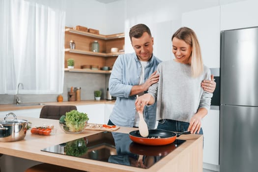 Frying food in a pan. Couple preparing food at home on the modern kitchen.