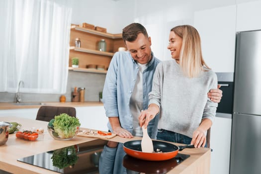 Frying food in a pan. Couple preparing food at home on the modern kitchen.