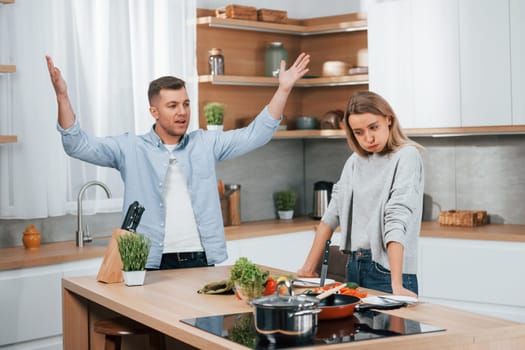 Arguing with each other. Couple preparing food at home on the modern kitchen.
