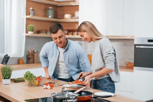 Using vegetables. Couple preparing food at home on the modern kitchen.