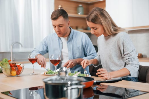 With glasses of wine. Couple preparing food at home on the modern kitchen.