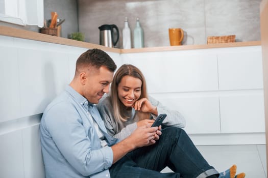 Couple sitting on the floor of modern kitchen.