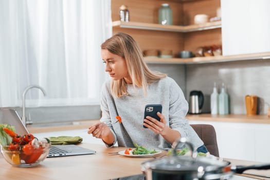 Holding phone. Woman preparing food at home on the modern kitchen.