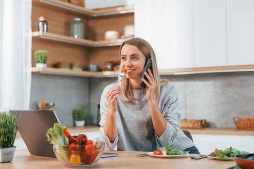 Holding phone. Woman preparing food at home on the modern kitchen.