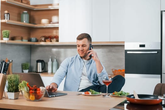 Using laptop. Man preparing food at home on the modern kitchen.