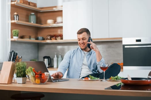 Talking by phone. Man preparing food at home on the modern kitchen.
