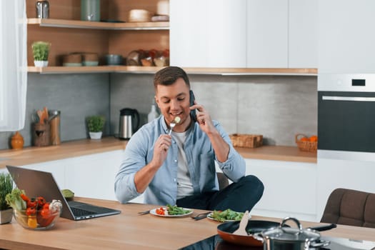 Talking by phone. Man preparing food at home on the modern kitchen.