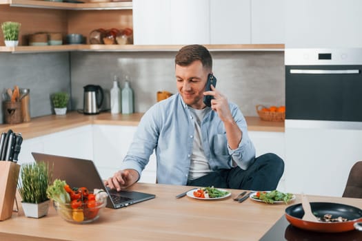 Talking by phone. Man preparing food at home on the modern kitchen.