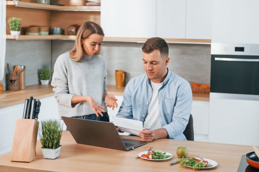 Using internet. Couple preparing food at home on the modern kitchen.