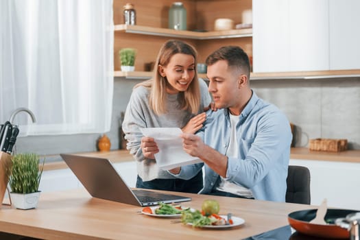 Using internet. Couple preparing food at home on the modern kitchen.