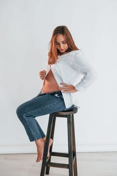 Pregnant woman is sitting on the chair in the studio.