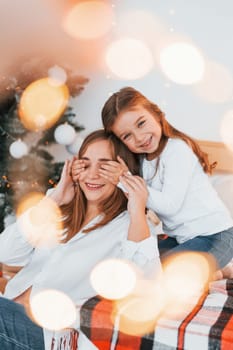 Mother with her little daughter is having fun indoors on the bed.