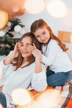 Mother with her little daughter is having fun indoors on the bed.