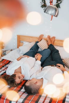 Laying down on the bed. Lovely couple celebrating holidays together indoors.