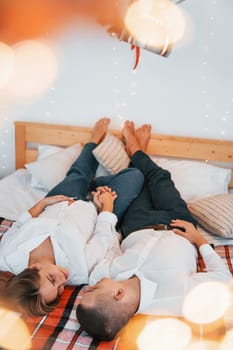 Laying down on the bed. Lovely couple celebrating holidays together indoors.