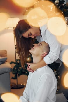 Embracing each other. Lovely couple celebrating holidays together indoors.